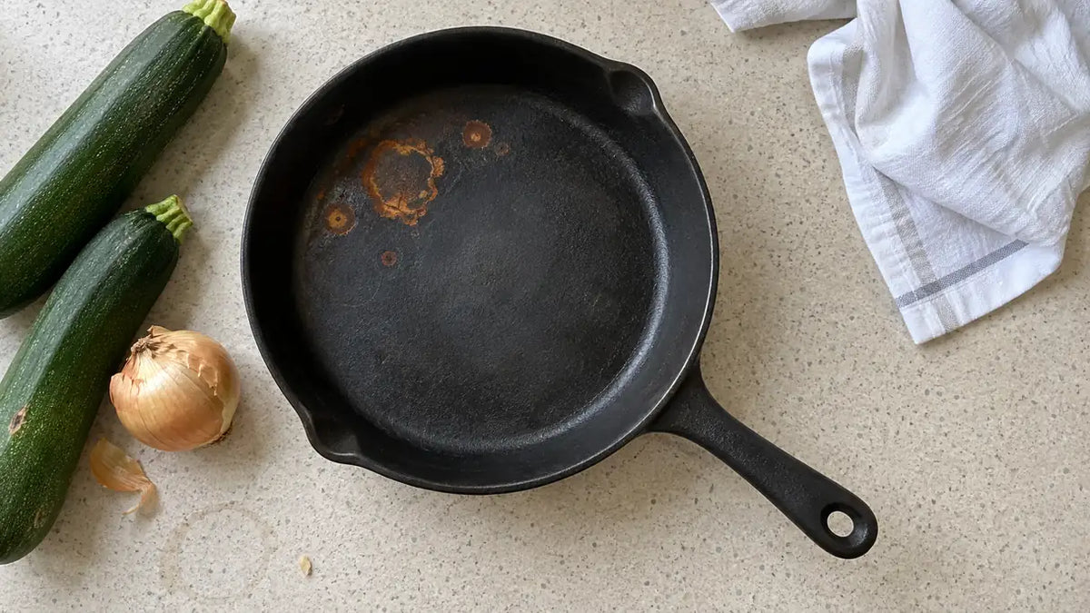 La fonte rouille-t-elle : taches de rouille orange sur la surface de cuisson d'une poêle en fonte, courgettes et oignon à côté