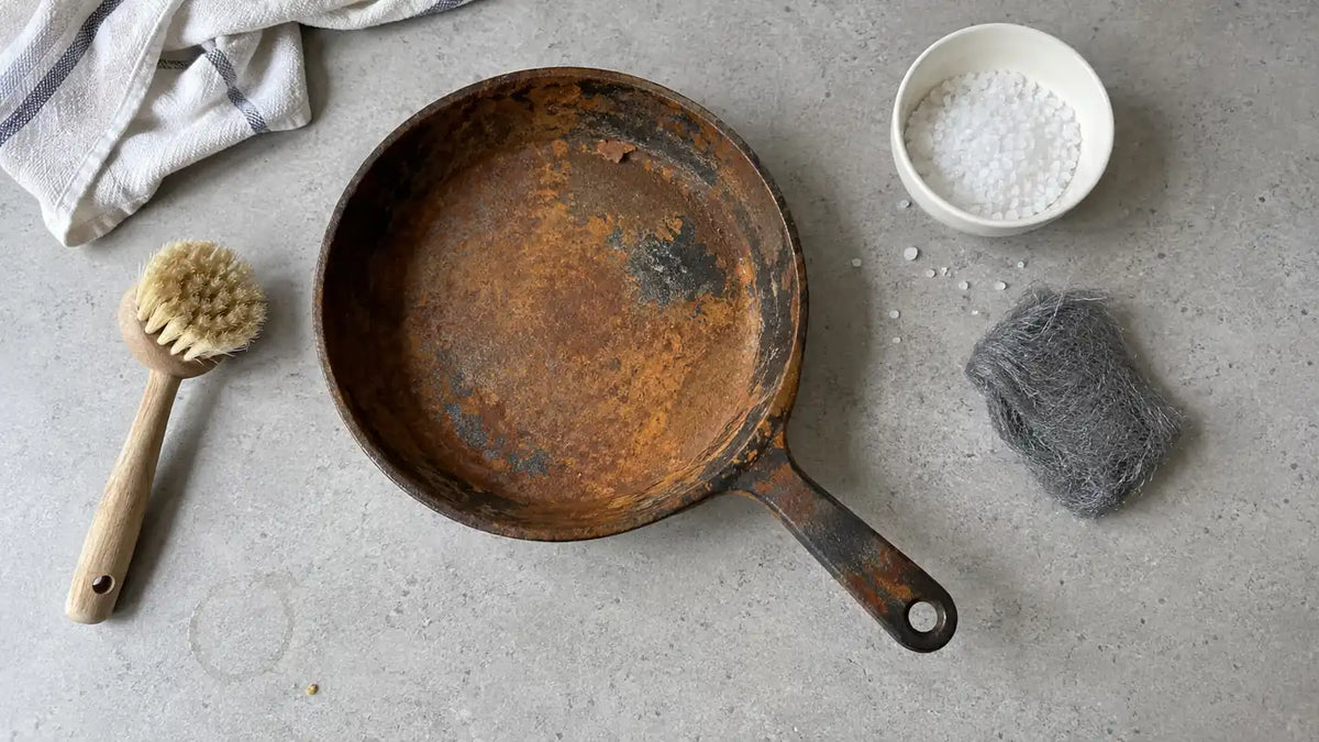 Nettoyer une poêle en fonte rouillée : une vieille poêle couverte de rouille, une brosse à vaisselle, du gros sel et une laine d'acier très fine