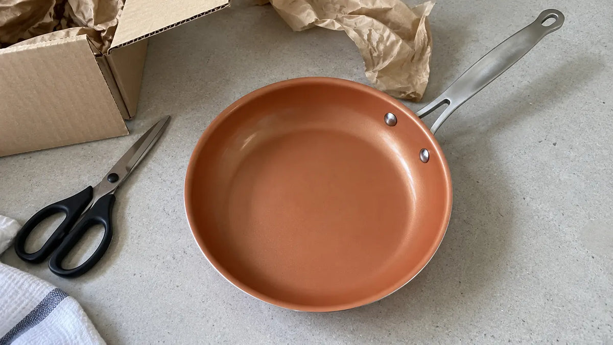 Poêle anti-adhérente en céramique couleur terre cuite tout juste sortie de son carton, avec le papier kraft et les ciseaux