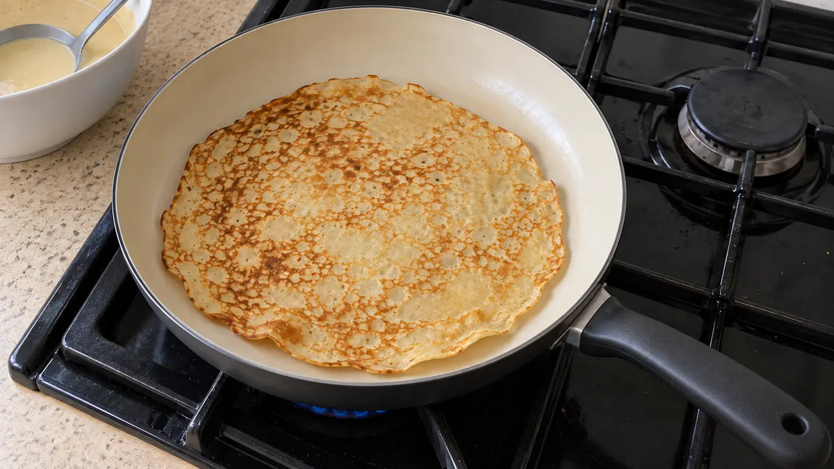 Poêle en céramique qui n'accroche pas : une crêpe dorée tout juste retournée, libre dans la poêle posée sur le gaz