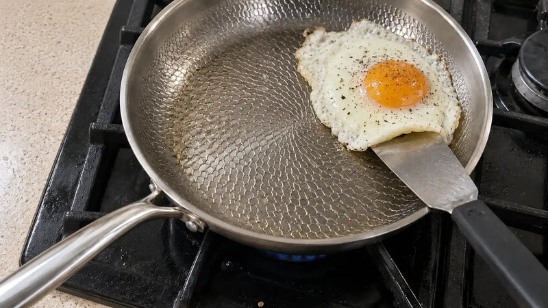Poêle en titane antiadhésive : une spatule soulève d'un seul morceau un œuf au plat qui n'accroche pas au métal martelé
