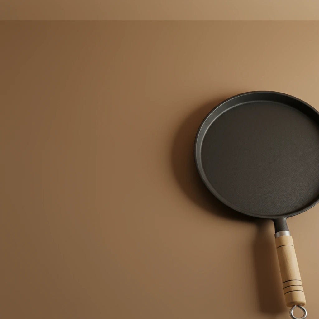 Poêle à crêpe en fonte 20 cm sur fond marron, vue de côté partielle mettant en valeur la surface de cuisson.