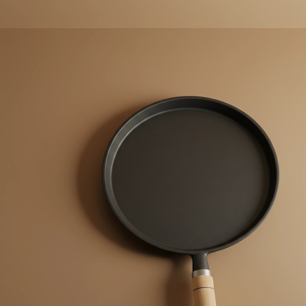 Poêle à crêpe en fonte 23 cm vue de dessus sur fond beige uni. Surface de cuisson noire mat et manche en bois clair.