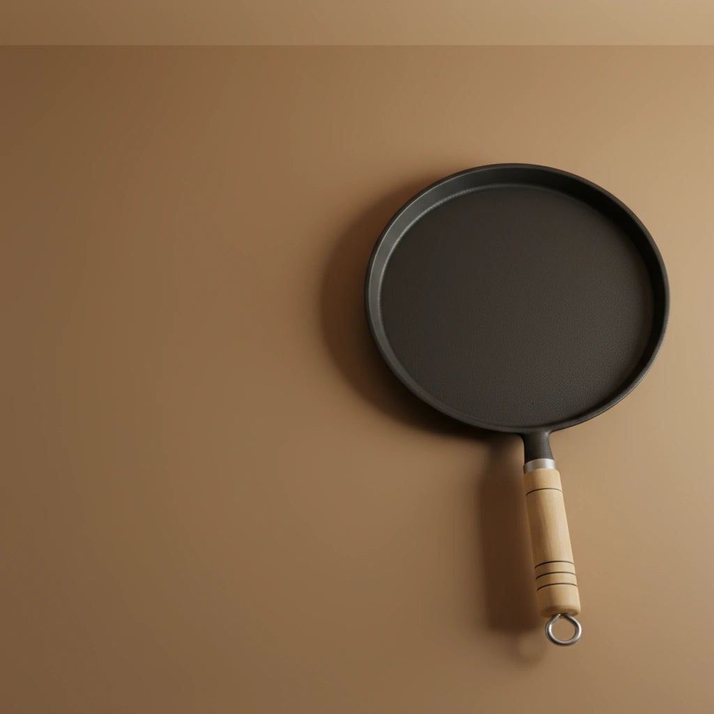 Poêle à crêpe en fonte 23 cm sur fond uni, montrant le manche en bois avec l'anneau de suspension.