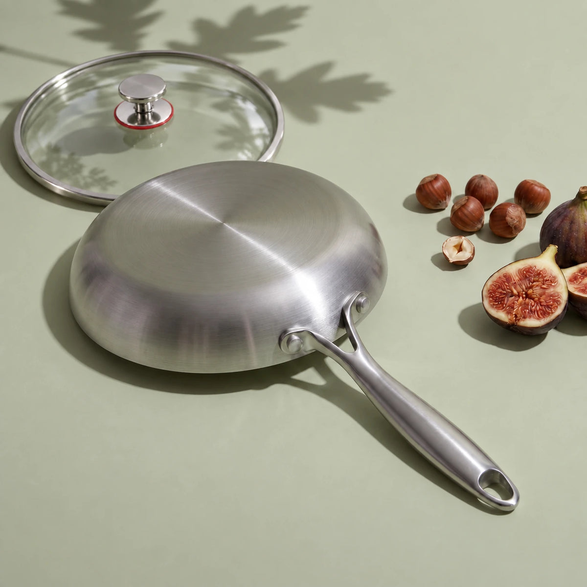 Dessous plat de la poêle en titane 26 cm avec couvercle, retournée près de son couvercle en verre, de noisettes et de figues