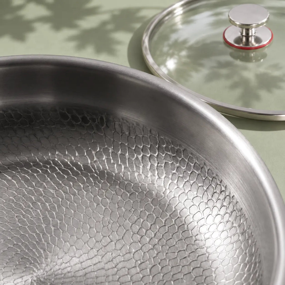 Gros plan sur la surface de cuisson texturée de la poêle en titane 26 cm avec couvercle, le couvercle en verre posé derrière