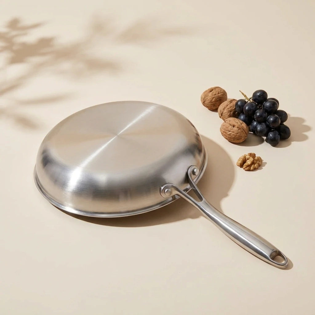 Poêle en titane 26 cm retournée, son dessous en inox lisse à côté de noix et de raisins noirs sur fond crème
