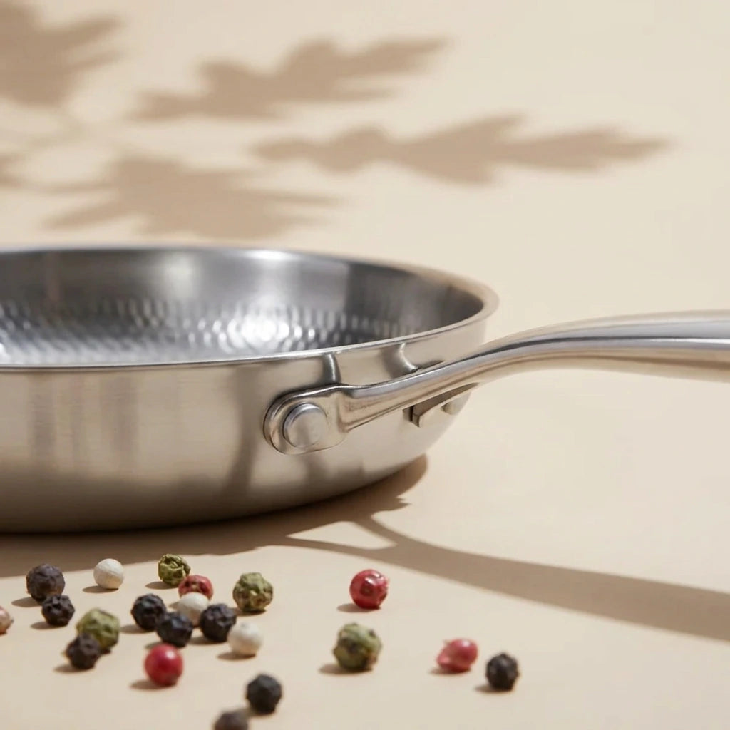 Poêle en titane 26 cm de profil, son manche riveté au-dessus de grains de poivre multicolores sur fond crème