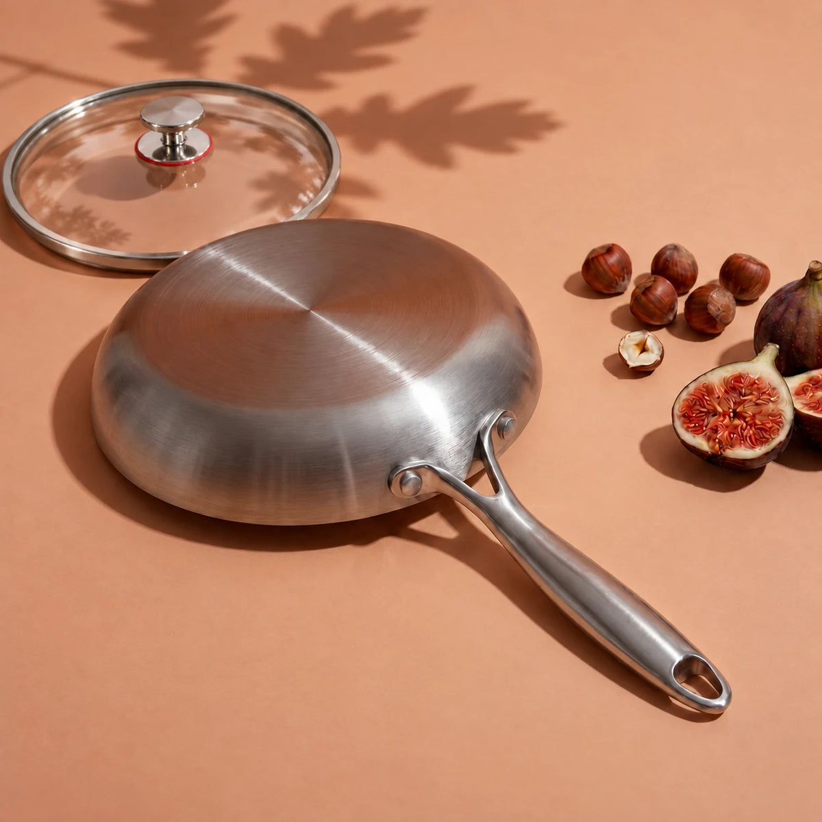 Dessous plat de la poêle en titane 28 cm avec couvercle, retournée près de son couvercle en verre, de noisettes et de figues