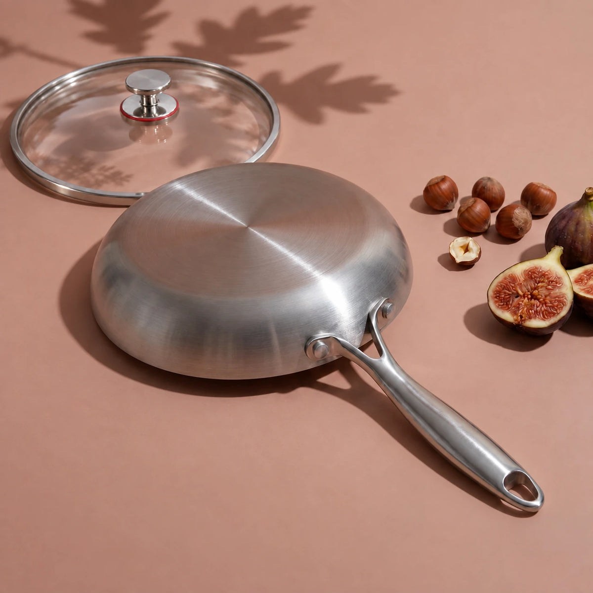 Dessous plat de la poêle en titane 30 cm avec couvercle, retournée près de son couvercle en verre, de noisettes et de figues
