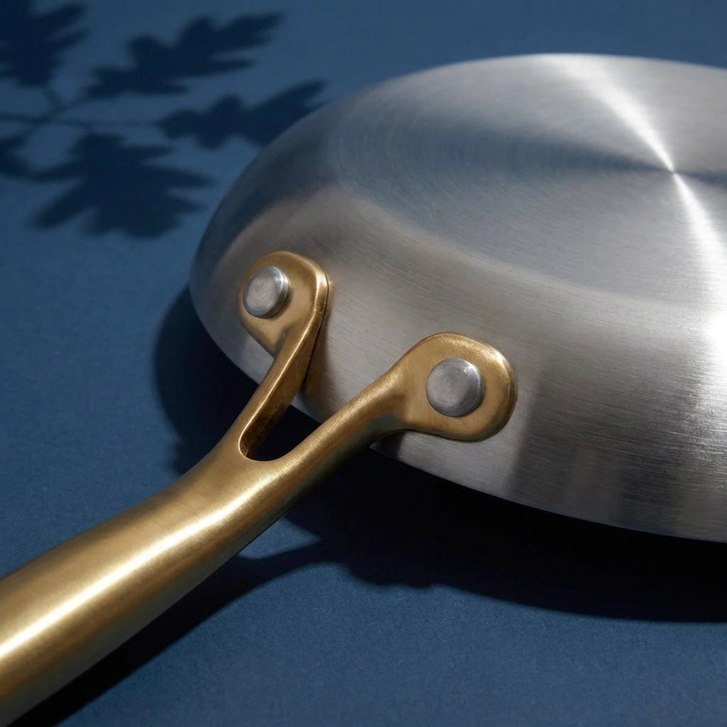 Dessous brossé de la poêle tous feux 26 cm, avec la fourche de son manche doré et ses deux rivets