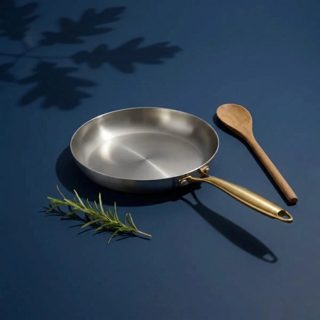 Poêle tous feux 26 cm vue en plongée, sa surface de cuisson brossée, avec du romarin et une cuillère en bois