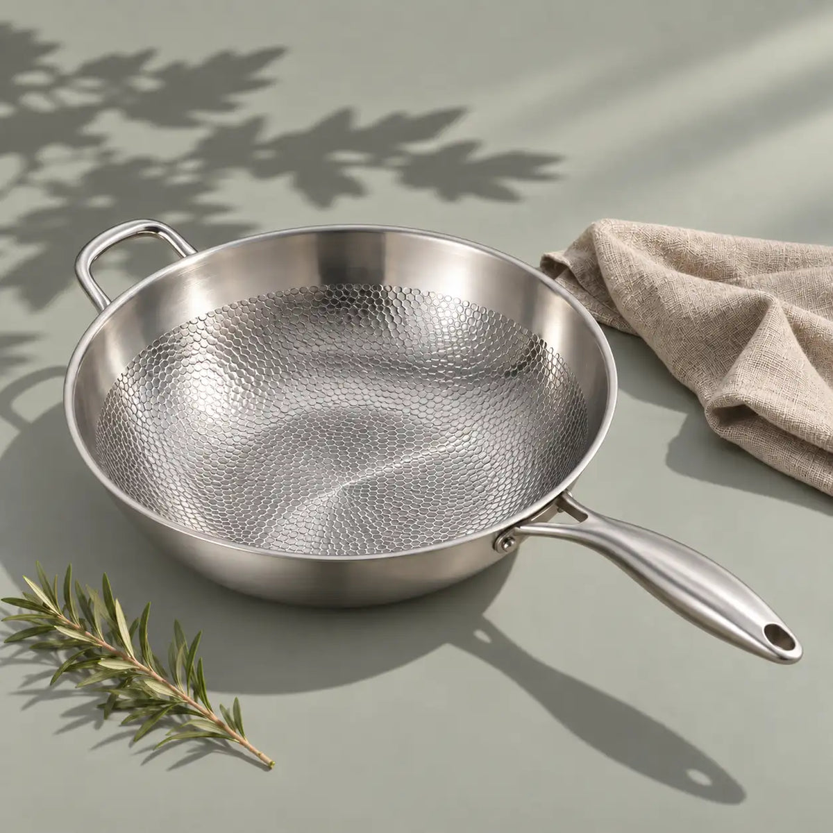 Wok en titane 32 cm vu de dessus avec son long manche, sa contre-poignée et sa surface martelée, un torchon en lin à côté