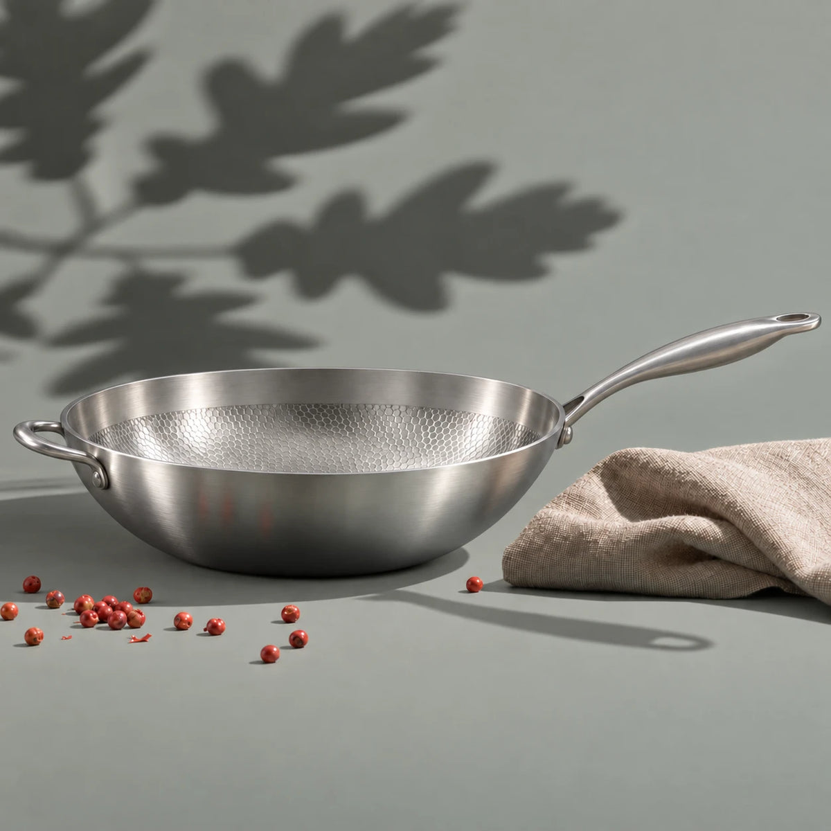 Wok en titane martelé 32 cm vu de profil, ses bords hauts de 8,5 cm et son long manche, des baies roses et un torchon à côté