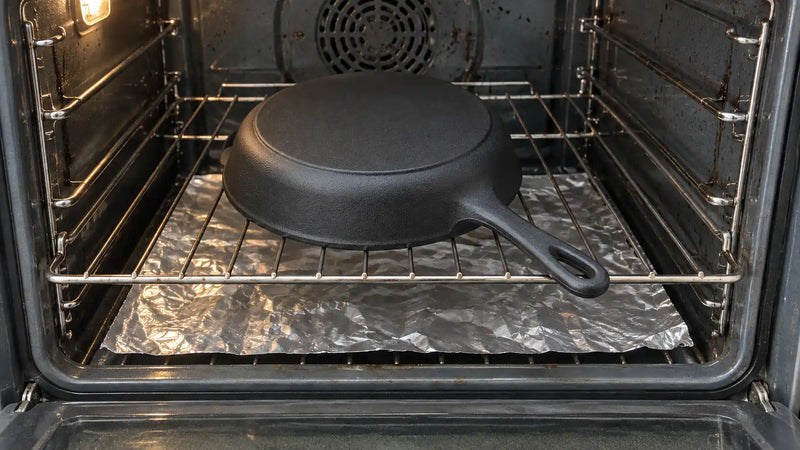 Comment culotter une poêle en fonte : la poêle posée à l'envers sur la grille du four, au-dessus d'une feuille d'aluminium