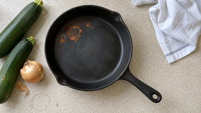 La fonte rouille-t-elle : taches de rouille orange sur la surface de cuisson d'une poêle en fonte, courgettes et oignon à côté