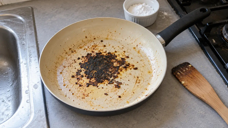 Nettoyer une poêle en céramique brûlée : une croûte noire au centre, du bicarbonate et une spatule en bois près de l'évier