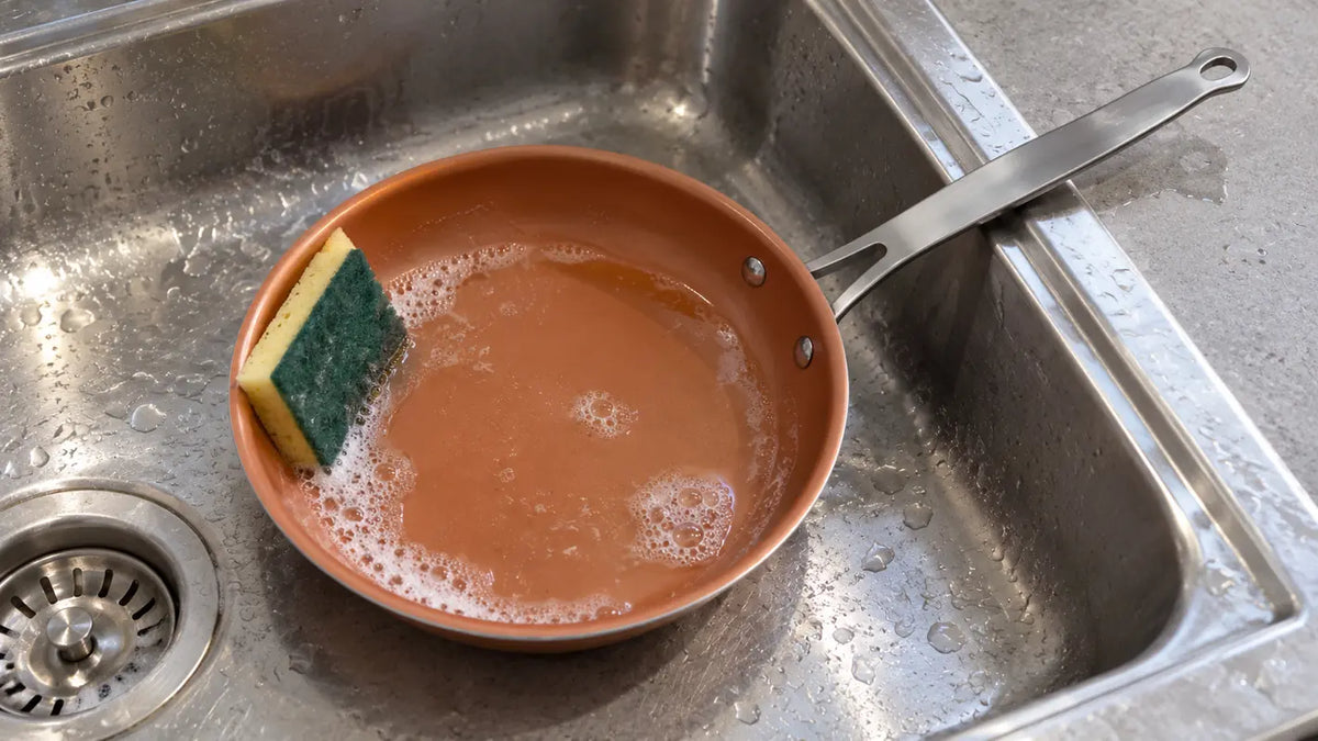 Nettoyer une poêle en céramique : la poêle dans l'évier, avec un fond d'eau chaude savonneuse, le côté doux de l'éponge posé contre son revêtement
