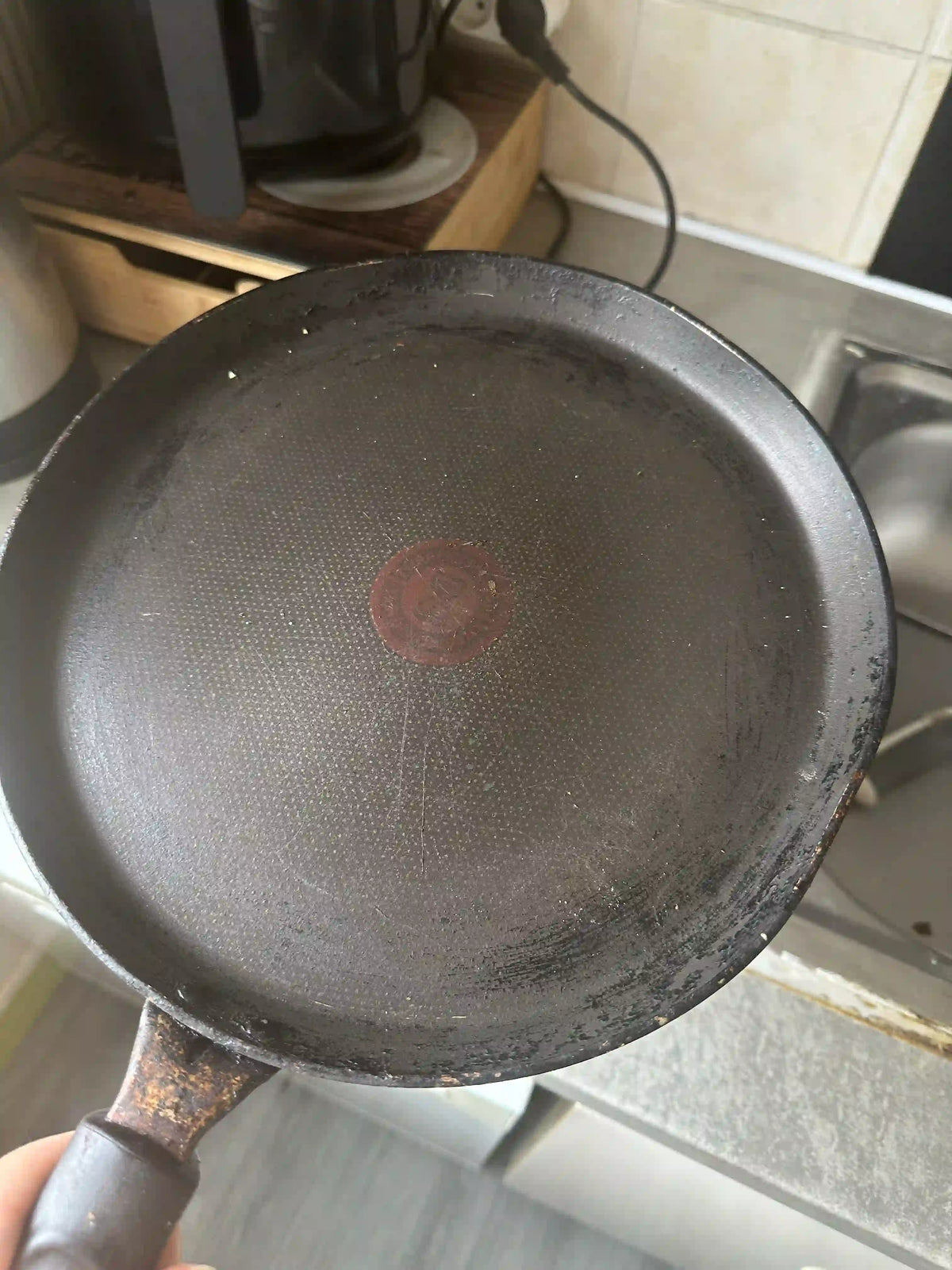 Poêle rayée tenue à la main, au revêtement antiadhésif usé et terni au centre par les cuissons