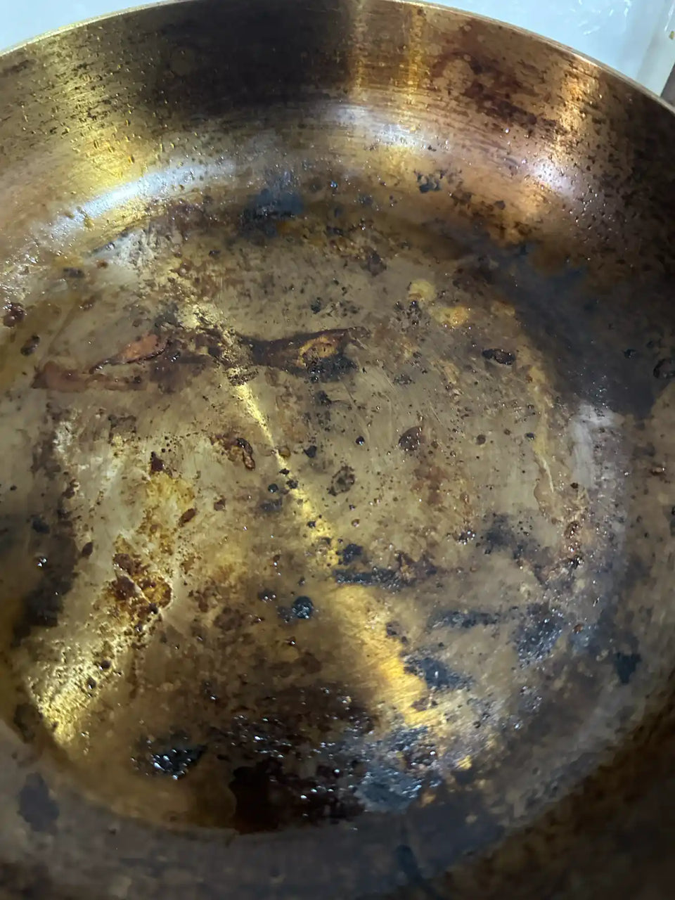 Fond d'une poêle en inox vu de près, avec un voile brun de graisse cuite et des résidus sombres attachés après une cuisson