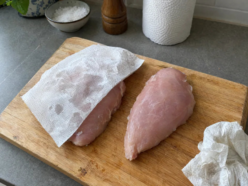 Blancs de poulet crus séchés au papier absorbant sur une planche en bois, avant la cuisson dans une poêle en inox