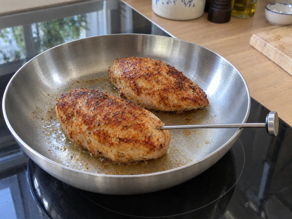 Thermomètre de cuisine à sonde piqué au cœur d'un blanc de poulet doré pour vérifier sa cuisson dans une poêle en inox