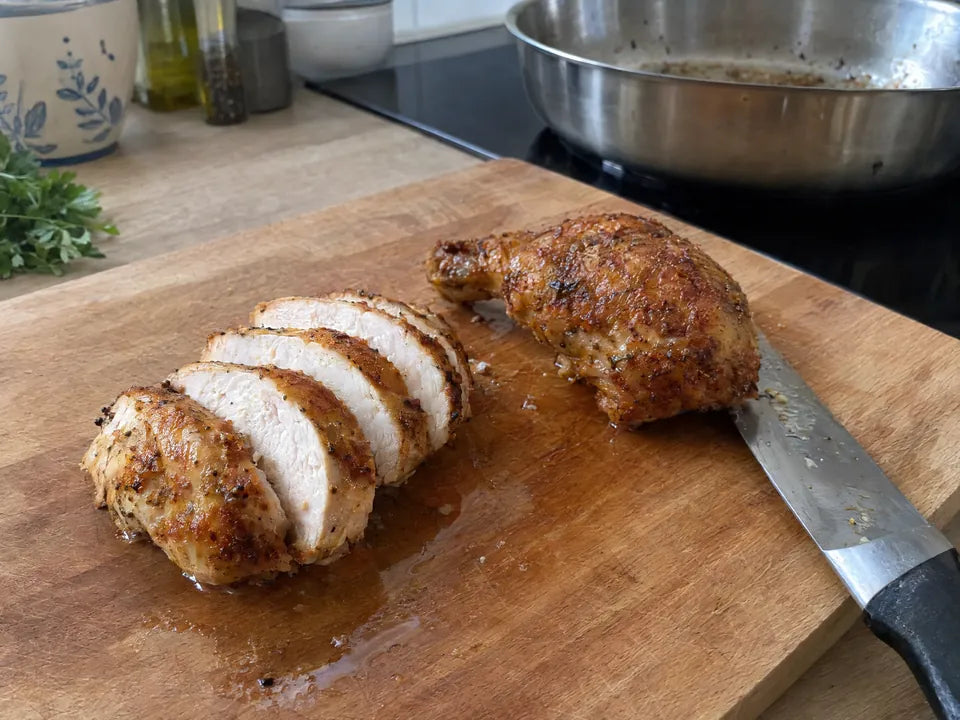 Blanc de poulet cuit à la poêle inox, tranché, juteux et blanc à cœur, à côté d'une cuisse de poulet dorée