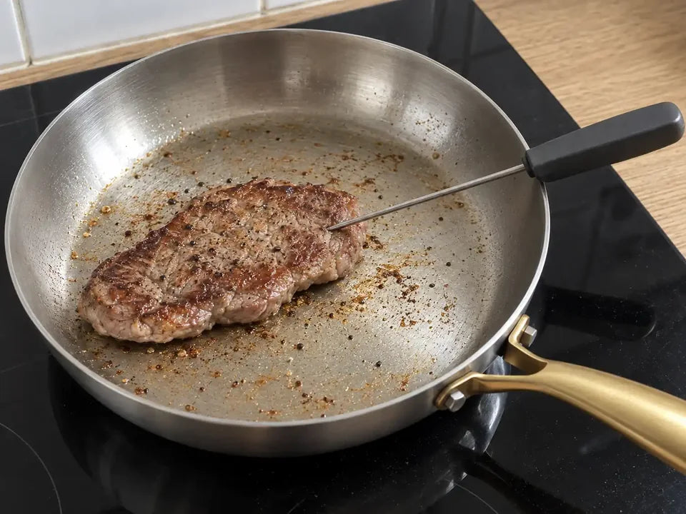 Thermomètre à sonde planté au cœur d'un steak pour vérifier la cuisson de la viande dans une poêle en inox
