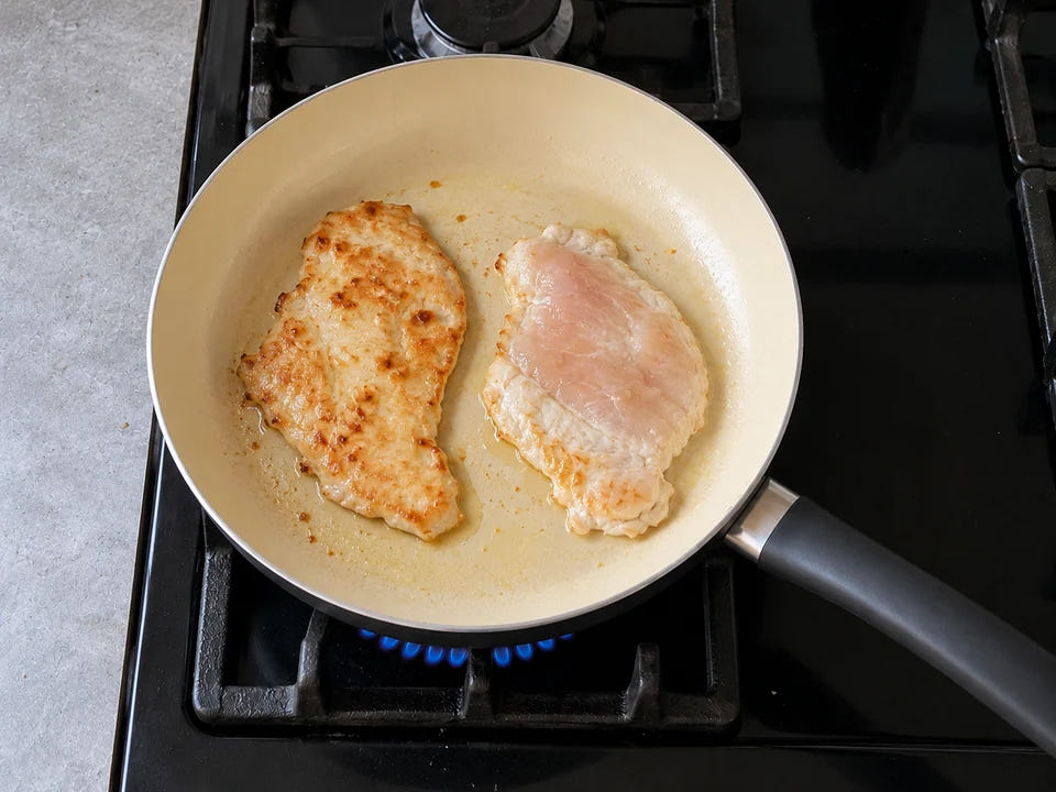 Cuisson dans une poêle en céramique : deux escalopes de poulet fines qui dorent à feu moyen, l'une déjà retournée