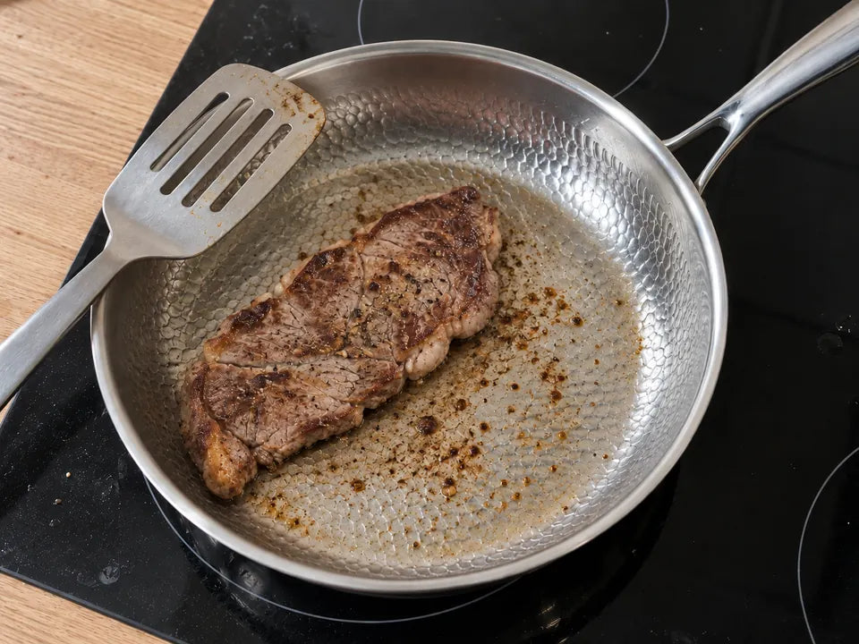 Entrecôte retournée dans une poêle en titane martelé : sa croûte est bien dorée et une spatule en métal repose sur le bord