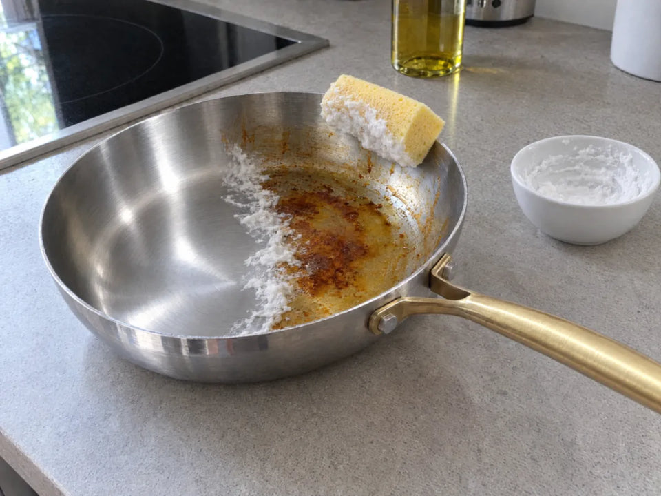 Déculotter une poêle en inox au bicarbonate de soude : une moitié encore tachée d'huile cuite, l'autre de nouveau brillante