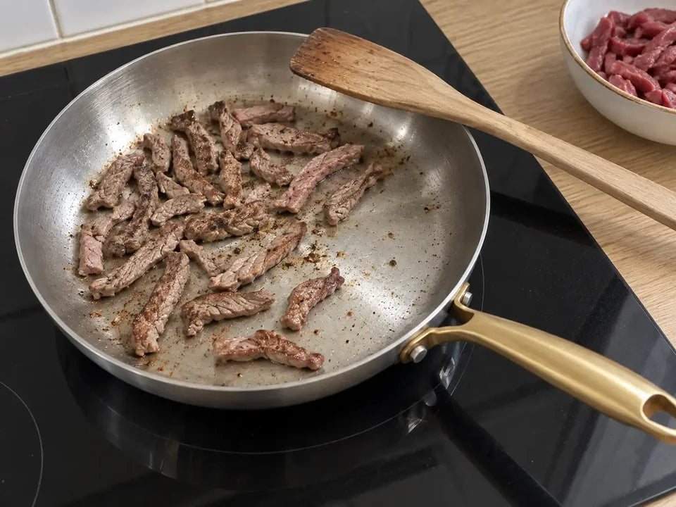 Émincés de bœuf saisis en une seule couche dans une poêle en inox, une spatule en bois posée sur le bord