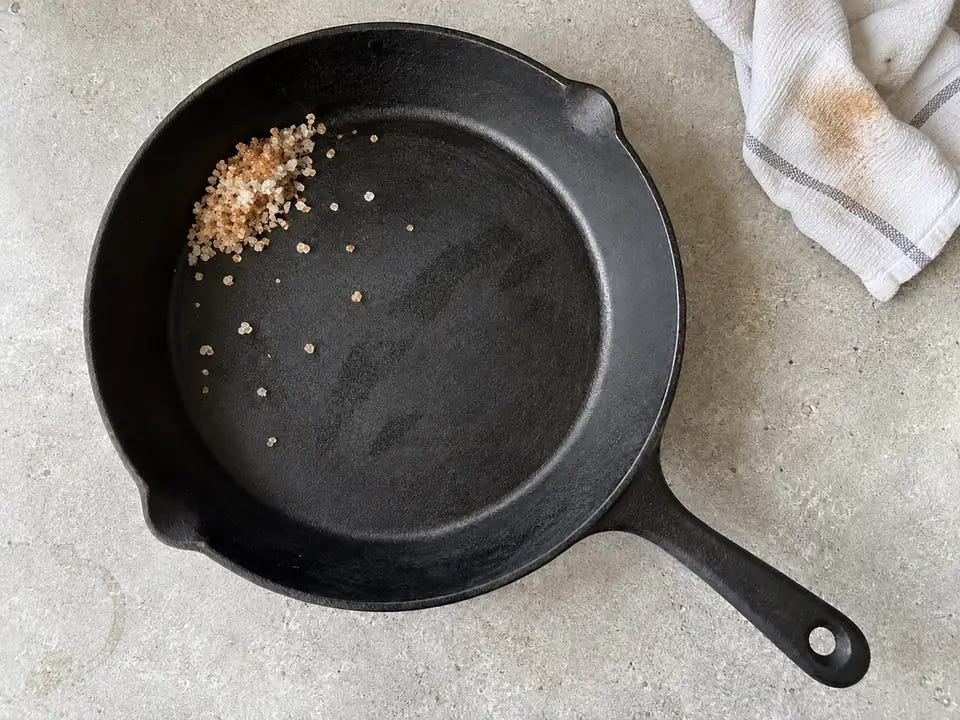 Enlever la rouille d'une poêle en fonte au gros sel : les points de rouille ont disparu et le sel teinté d'orange est poussé contre le bord