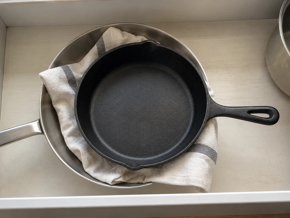 Entretenir une poêle en fonte : poêle rangée bien sèche dans un tiroir, un torchon glissé entre elle et une poêle en inox