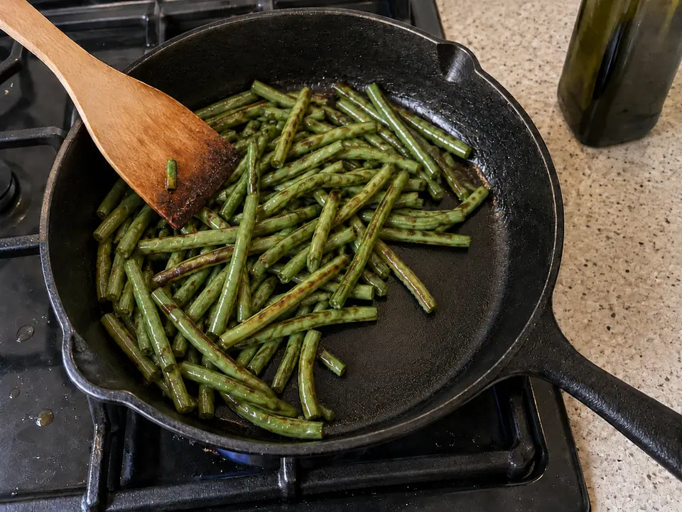 Huile pour cuisiner dans une poêle en fonte : des haricots verts qui dorent dans un filet d'huile d'olive, sur le gaz