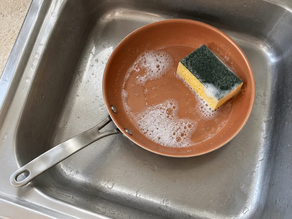 Laver une poêle en céramique : la poêle tiède lavée à l'eau chaude avec le côté doux d'une éponge, dans l'évier