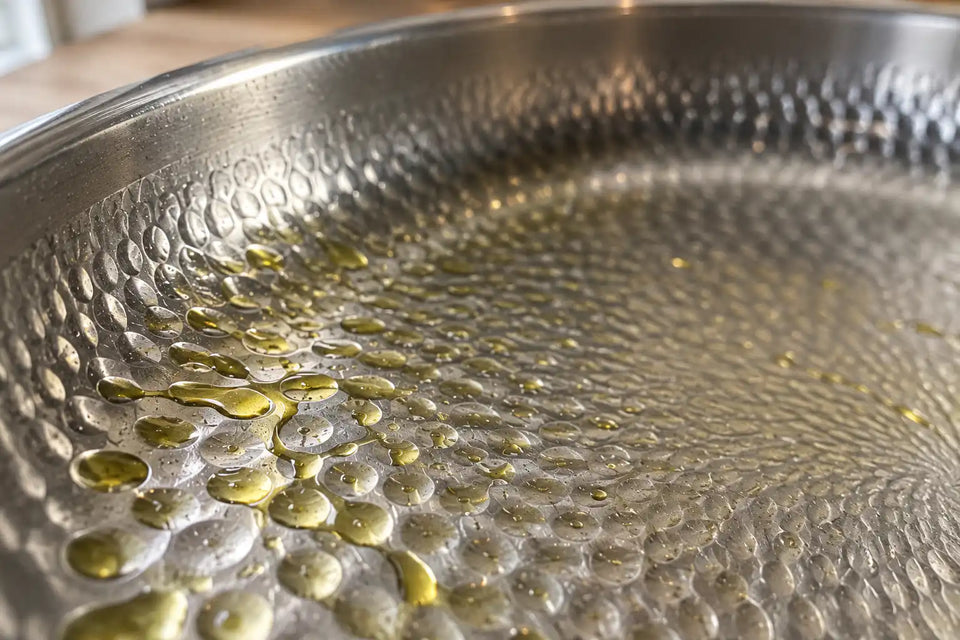 Gros plan sur la surface martelée d'une poêle en titane, un filet d'huile retenu dans les petites alvéoles