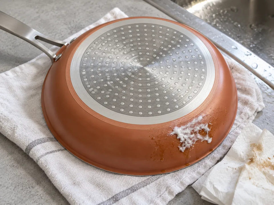 Nettoyer le dessous d'une poêle en céramique : de la pâte de bicarbonate sur une tache de l'extérieur, à côté du disque de métal pour l'induction