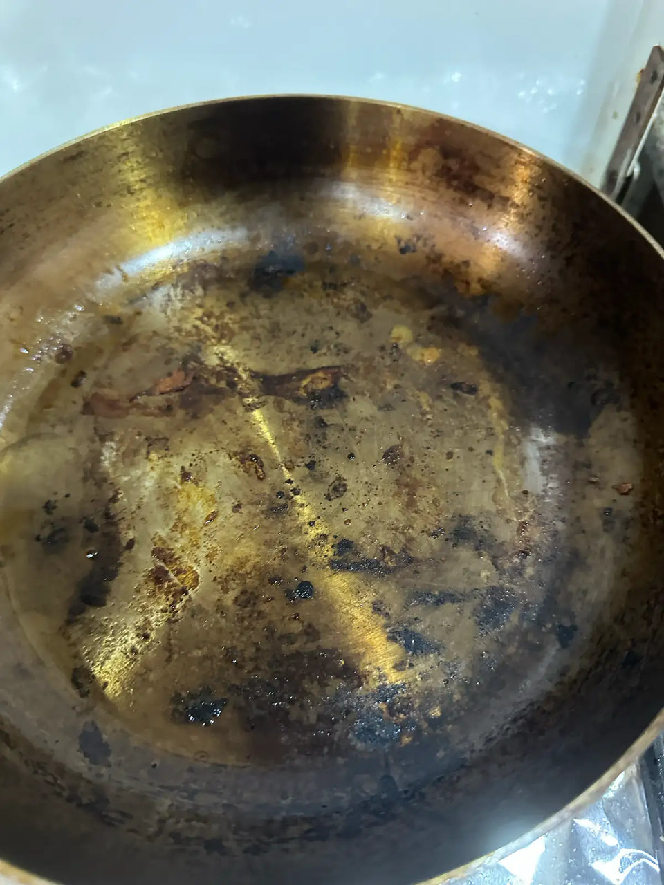 Gros plan sur une poêle en inox brûlée : reflets dorés du métal chauffé et résidus carbonisés au fond