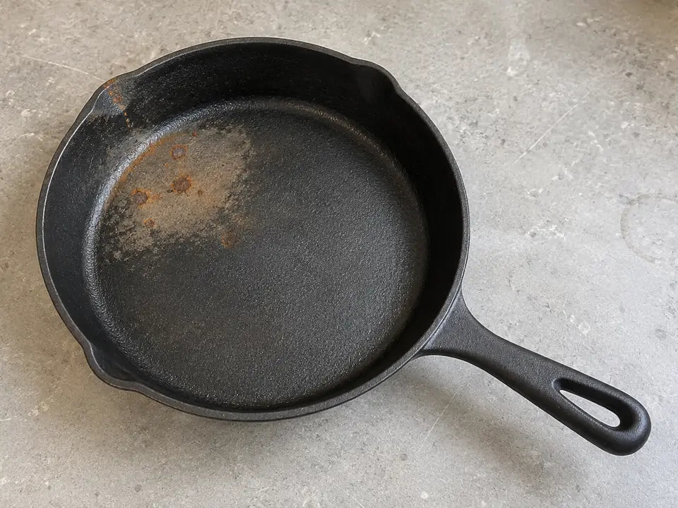 Poêle en fonte rouillée à nettoyer : quelques points de rouille orange et une zone terne sur sa surface de cuisson
