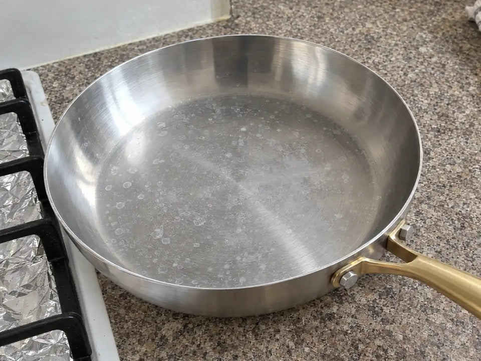 Taches blanches de calcaire sur une poêle en inox qui a séché à l'air, près d'une plaque de cuisson au gaz