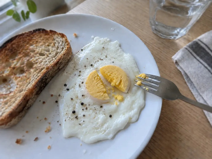 Œuf au plat au jaune bien cuit, coupé en deux à la fourchette dans une assiette blanche
