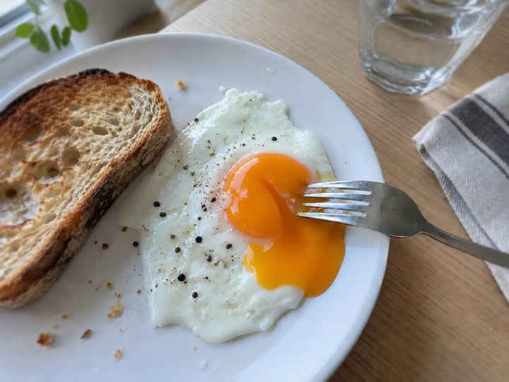 Œuf au plat au jaune coulant percé à la fourchette, servi avec une tartine de pain grillé