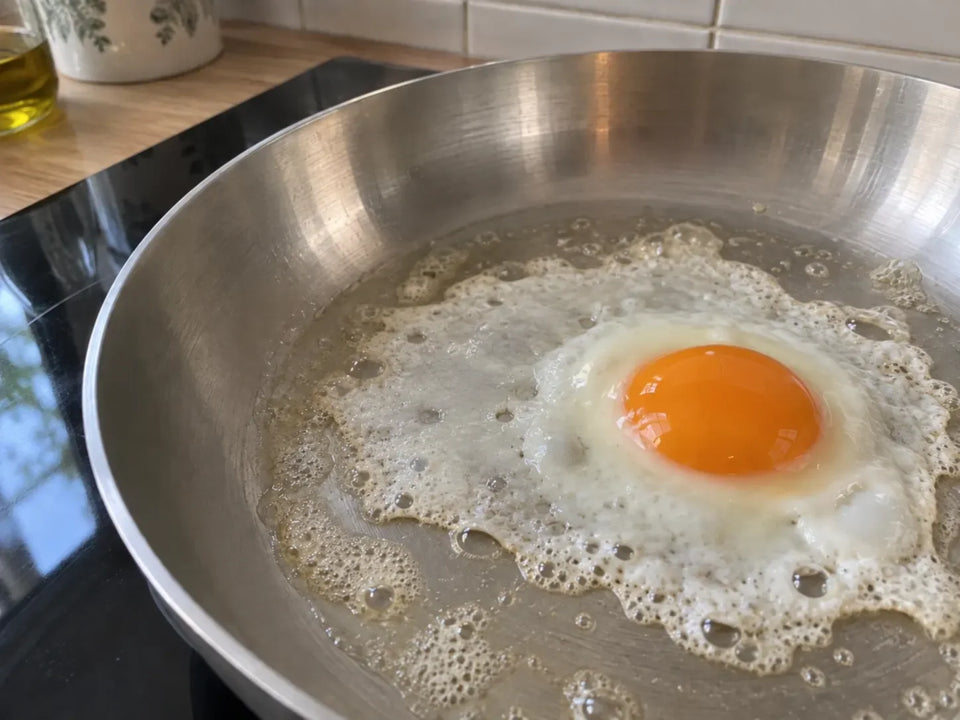 Œuf au plat moins frais dans une poêle inox : son blanc liquide s'étale en un voile fin et dentelé