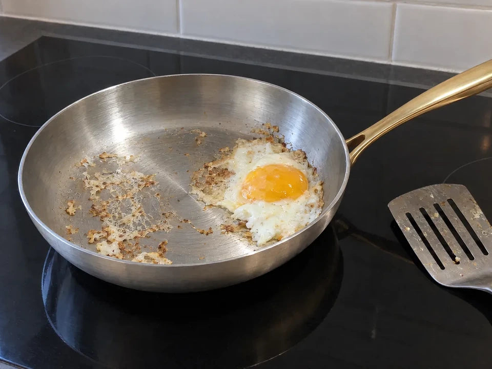 Œuf au plat raté qui a accroché et s'est déchiré dans une poêle inox, une spatule en métal posée à côté sur l'induction