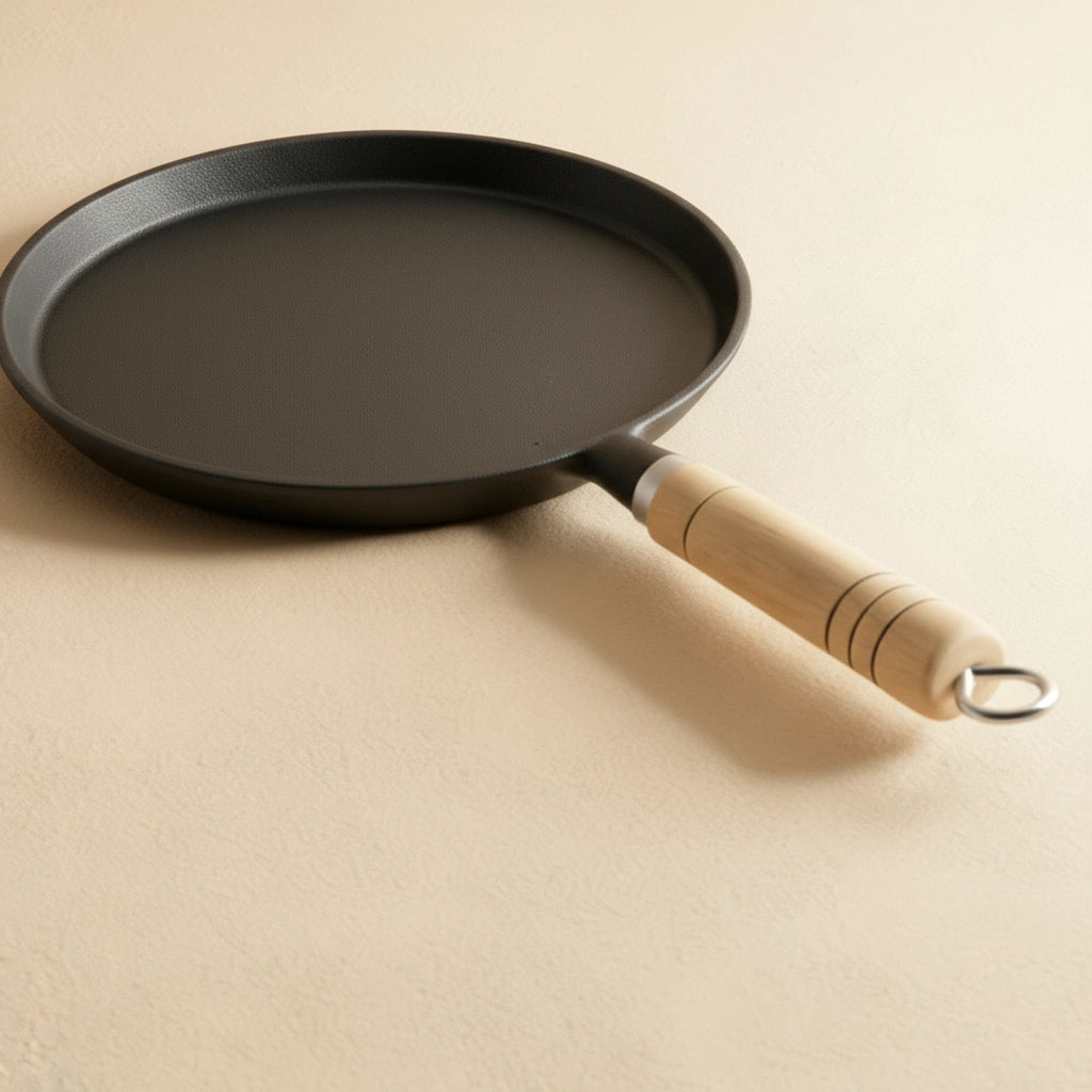 Gros plan en angle sur le corps de la poêle à crêpe en fonte 20 cm et le manche en bois clair.