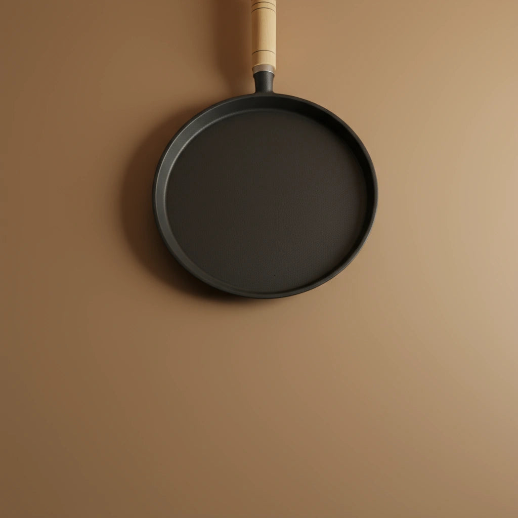 Poêle à crêpe en fonte 23 cm vue de dessus sur fond beige. Présente la surface de cuisson et le manche en bois.