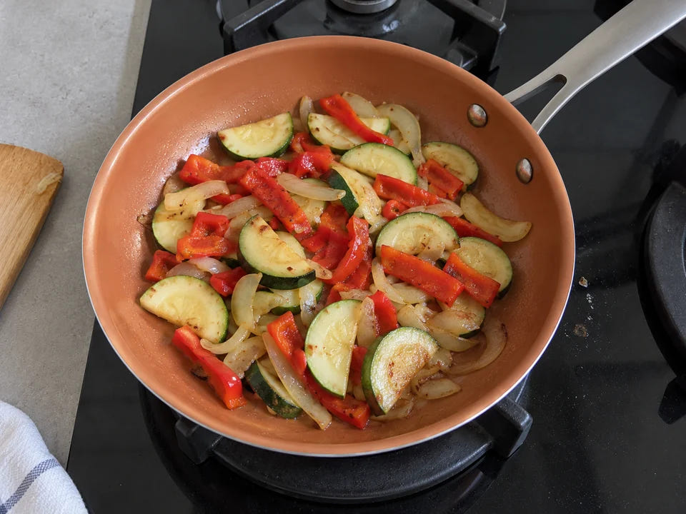 Poêle en céramique saine : des courgettes, des poivrons rouges et des oignons dorent avec un simple filet d'huile sur le gaz