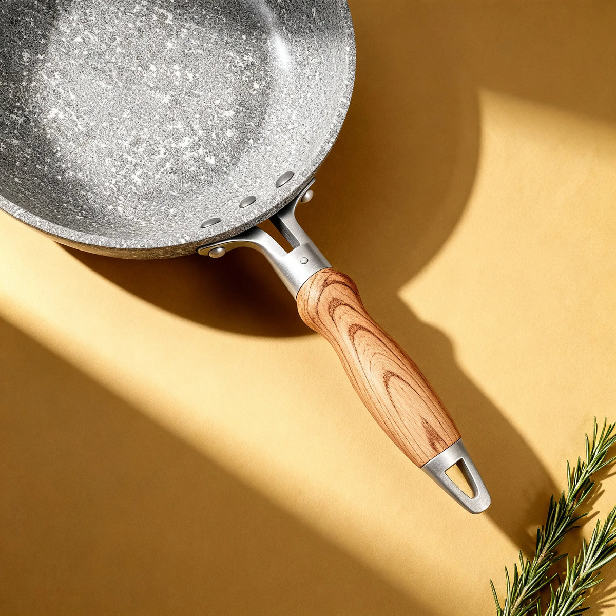 Poêle en aluminium induction 26 cm : vue de dessus avec le manche aspect bois et du romarin.
