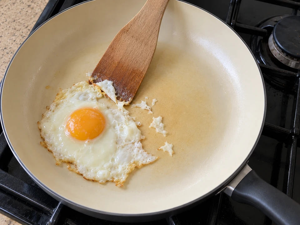 Poêle en céramique qui accroche : au centre, la pellicule d'huile cuite ambrée retient l'œuf au plat déchiré par la spatule
